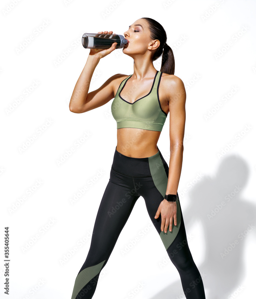 Resting time. Sweaty girl with opens bottle of water. Photo of girl with perfect body on white background. Strength and motivation Resting time. Sweaty girl with opens bottle of water. Photo of girl with perfect body on white background. Strength and motivation
