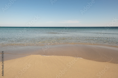 Calm Jonio Sea, Puglia, South Italy, the waves bathe the smooth golden sand in the golden hour, tropical image and clear sky.
