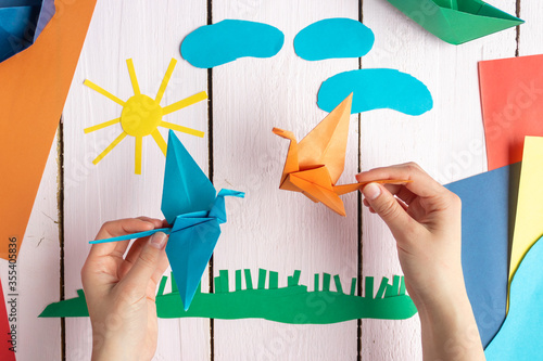A girl is playing with an origami crane made of paper that she made herself. On a wooden background