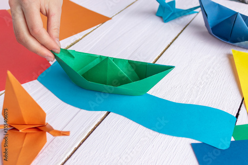 The girl is playing with origami of a paper boat that she made herself. On a wooden background