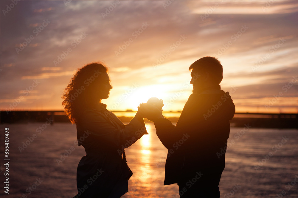 Love, affection and romantic relationship. Happy caucasian young couple in love stand face to face and holding hands and crystall ball on sunset river beach.