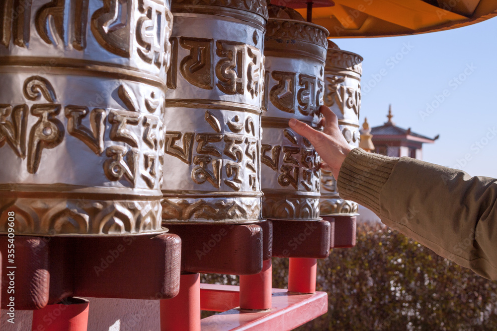 Hand moving buddhist prayer wheels with temple in the background.
