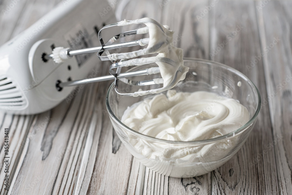 Woman whipping cream using electric hand mixer on the gray rustic wooden  table Stock Photo