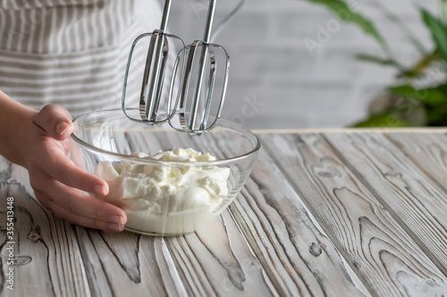 Obraz na plátně Woman whipping cream using electric hand mixer on the gray rustic wooden table
