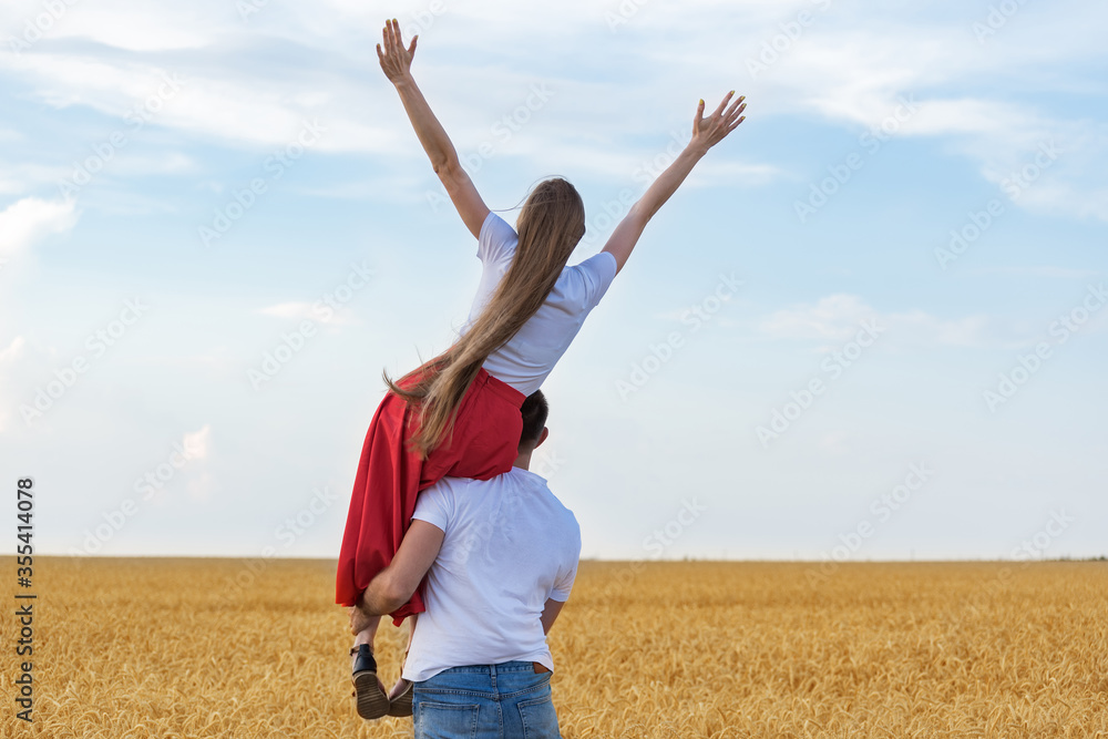 Rear view of a young couple in wheat field. Man holding woman on his shoulder Rear view of a young couple in wheat field. Man holding woman on his shoulder