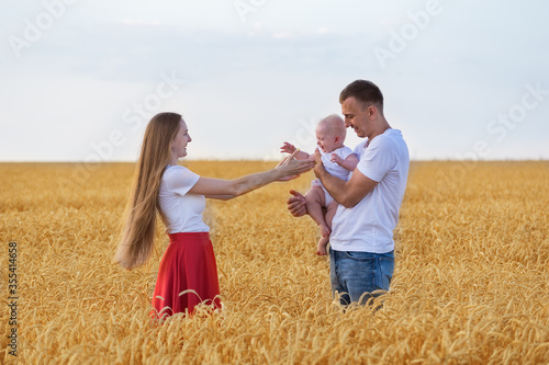 Happy young parents playing with baby in field. Mom, dad and kid having fun outdoors