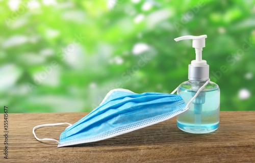 Coronavirus prevention medical  masks and bottle hand sanitizer gel alcohol on wooden table with blurred green nature background. 
Concept Covid-19 protection.