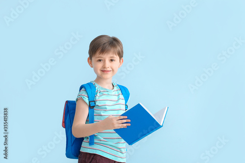 Bilde på lerret Cute little schoolboy with book on color background
