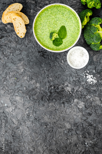 Broccoli cream soup, bread, spoon on grey kitchen desk top-down copy space