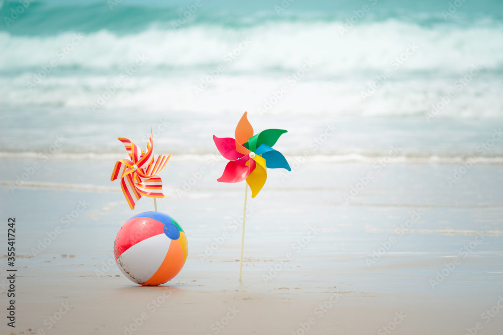 Obraz premium Colorful ball and paper windmill on sandy summer tropical beach with blue sea