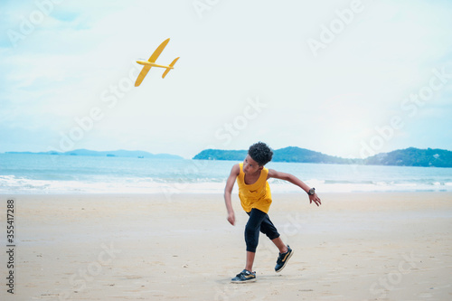 Cute kid having fun on sandy summer with blue sea, happy childhood boy playing model plane on tropical beach