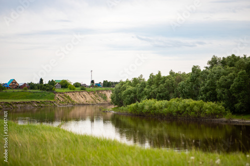 The village stands on a hill near the Tara river, Omsk region, Siberia. Private homes, rural area near the reservoir, on a cliff. The river flows through meadows and forests.