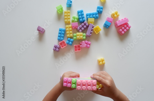 Close up of child's hands playing with colorful plastic bricks at the table. Toddler having fun and building out of bright constructor bricks. Early learning. stripe background. Developing toys