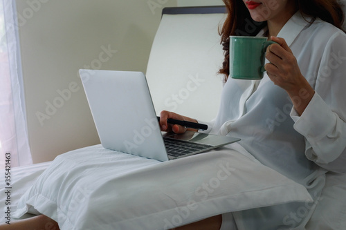 Relaxing work at home, concept with a women sitting on the bed with laptop and holding a coffee mug.