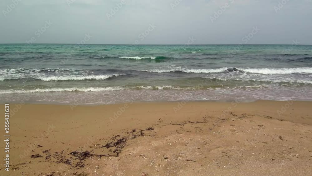 Low sideways flight right above brown sand at Kalogria beach with distant views of ocean and waves breaking on shore, Greece, aerial Low sideways flight right above brown sand at Kalogria beach with distant views of ocean and waves breaking on shore, Greece, aerial
