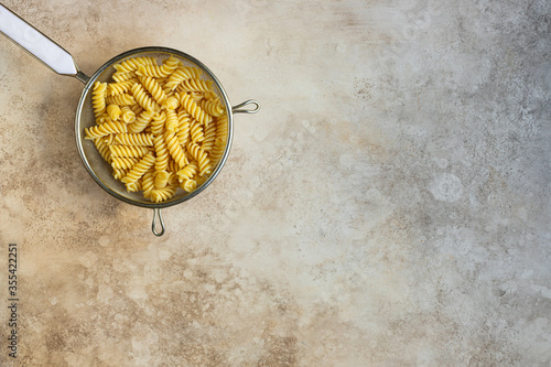 cooked fusilli in strainer top view. Italian pasta without sauce. beige neutral background, space for text