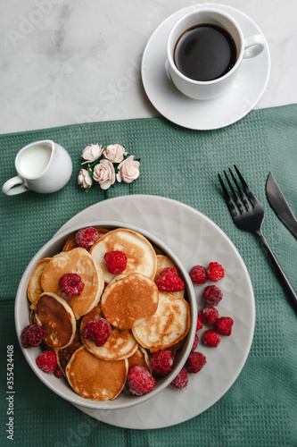 Trendy homemade Breakfast mini pancakes with raspberries and coffee on a white table. The view from the top. Side view. Space for text