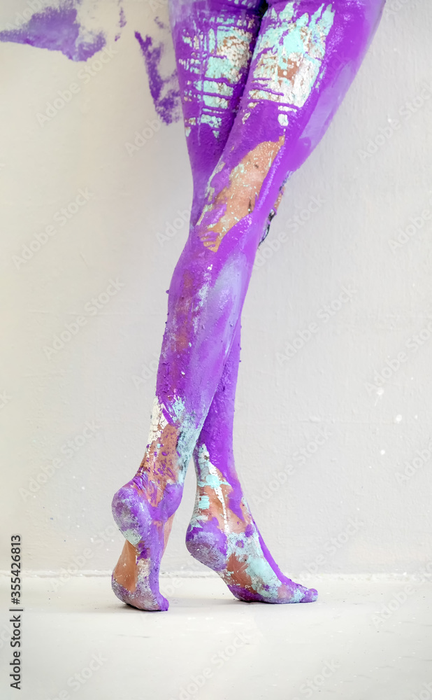 Fototapeta premium View from behind on beautiful legs and feet of a sexy young artistically abstract painted woman with white, blue and purple and paint. Creative body art painting, copy space.