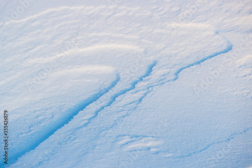 Beautiful winter background with snowy ground. Natural snow texture. Wind sculpted patterns on snow surface.