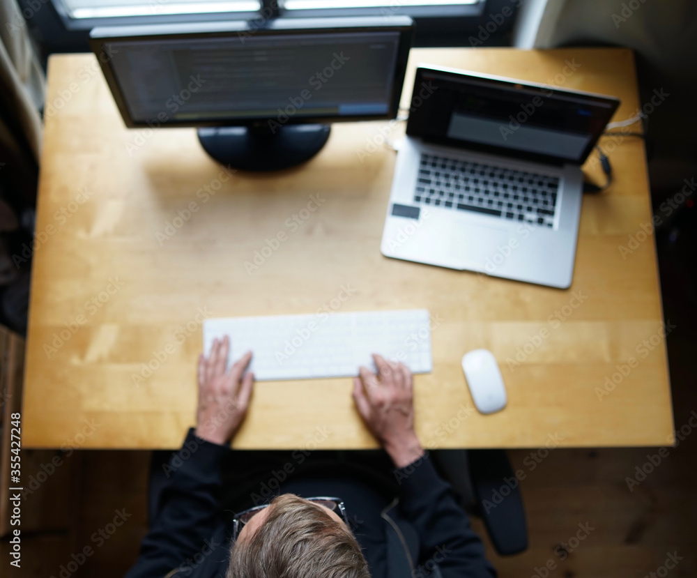 Top shot of programmer working with keyboard and mouse from home with laptop and external monitor. Top shot of programmer working with keyboard and mouse from home with laptop and external monitor.