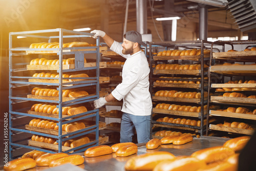 A baker carries a rack of bread at the bakery. Industrial bread production