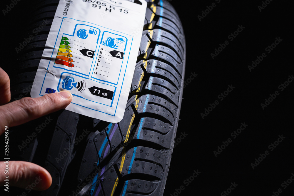 Label on tire with information about level of noise, braking distance on wet road, fuel efficiency. Finger shows on information sticker on tire.