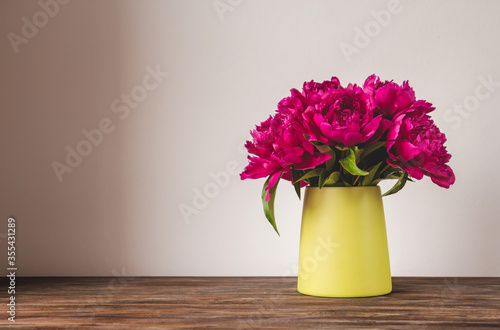 A bouquet of bright pink peonies in a green vase on a wooden table copy space. Blooming peonies. A bouquet of peonies as a gift.