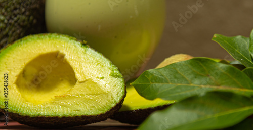 Glass bowl with avocado cream (Persea americana) between leaves and halved fruits photo