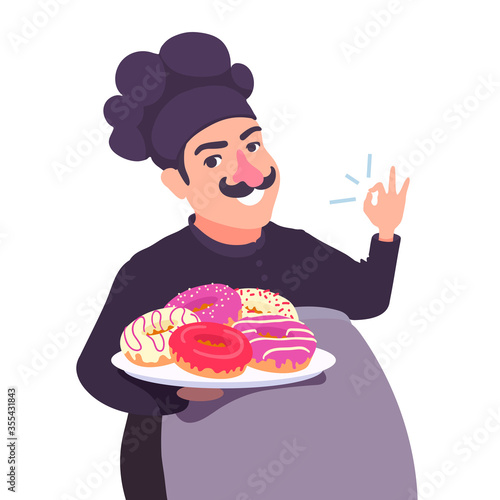 A cute confectioner baker holds a plate of various glazed doughnuts in his hand. A chef cook showing OK hand gesture, smiling. Delicious donuts.