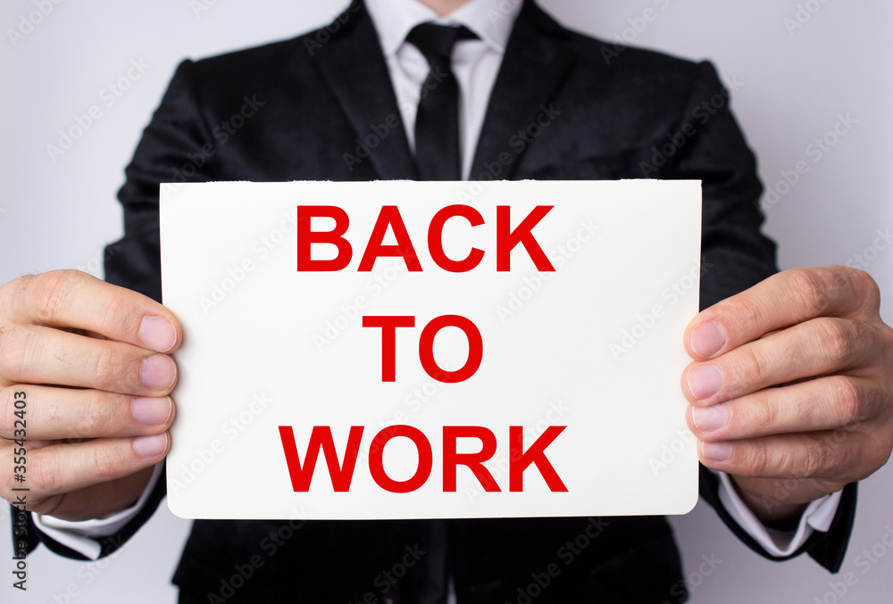 The inscription Back to work in red letters on a white sheet in the hands of a man in a business suit. The inscription Back to work in red letters on a white sheet in the hands of a man in a business suit.