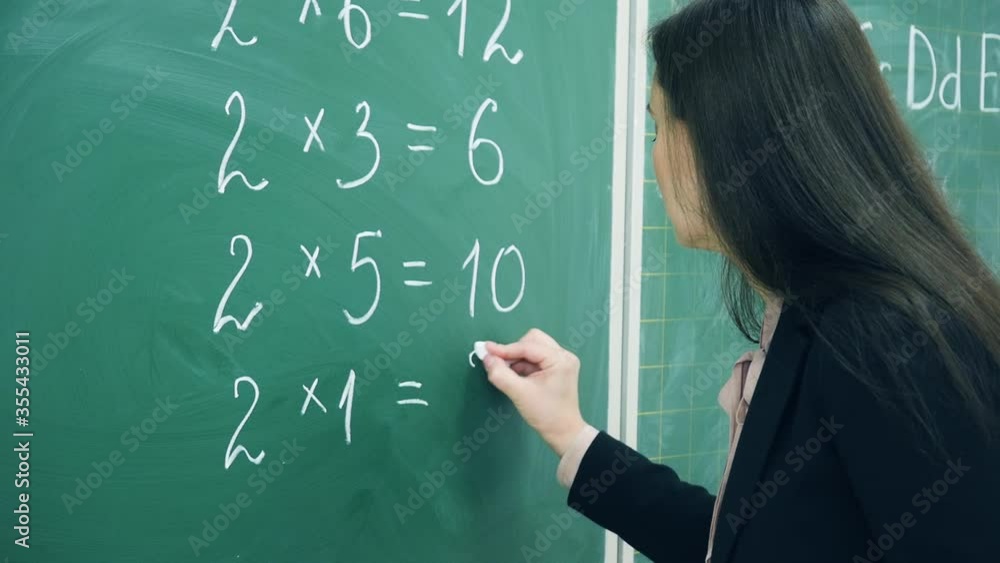 Elementary school. Teacher writing numbers on green chalk board in classroom. Education concept Elementary school. Teacher writing numbers on green chalk board in classroom. Education concept