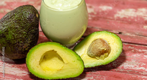 Glass bowl with avocado cream (Persea americana) between leaves and halved fruits photo