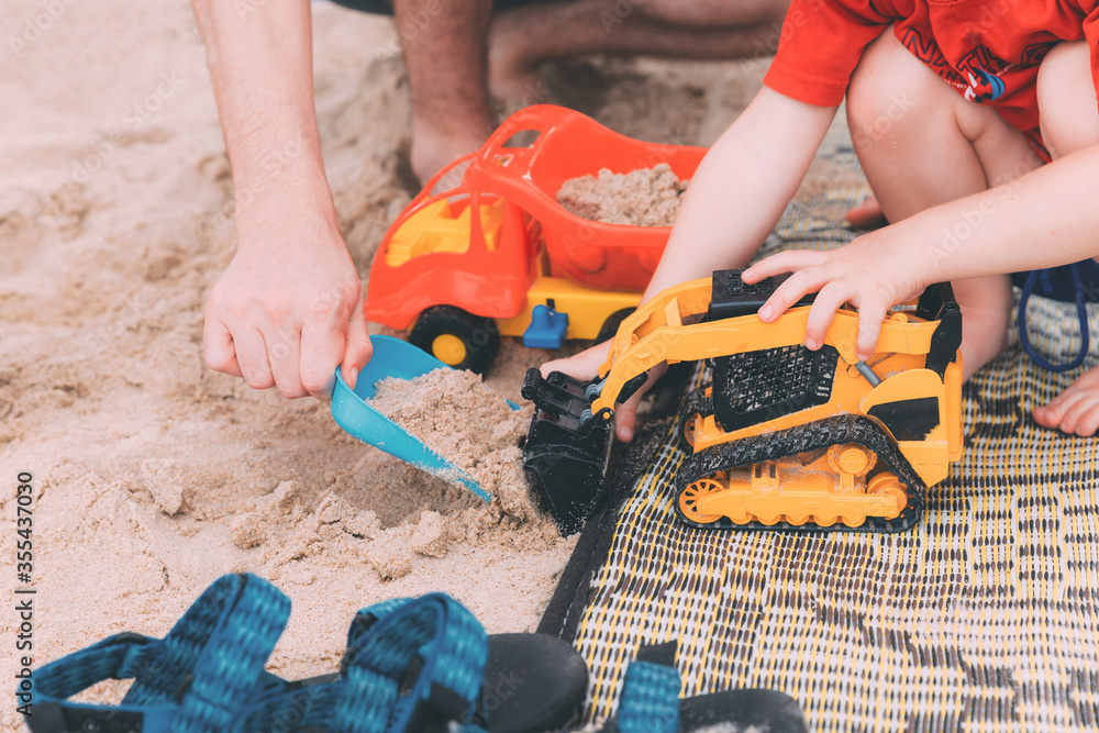 Father's day. Dad and son. Little son plays toys with dad on the beach with sand. Happy loving family. Happy family father and child. Toy cars. Hands of a man and a small child on the beach. Together