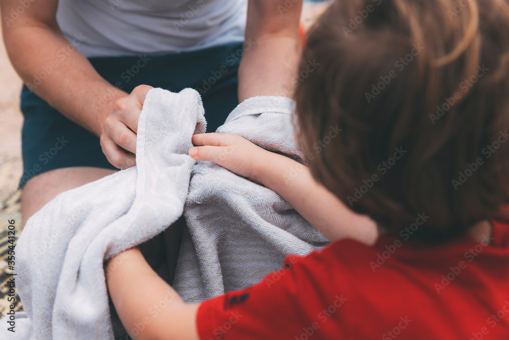 Father's day. Dad and son. Dad wipes his son's hands with a towel on the beach. Happy family father and child. Hands of a young man and his son blurred in the foreground from back. After washing hands Father's day. Dad and son. Dad wipes his son's hands with a towel on the beach. Happy family father and child. Hands of a young man and his son blurred in the foreground from back. After washing hands