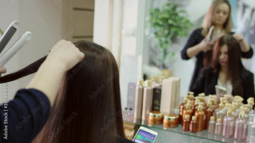 A slow motion close up shot of a blonde hair stylist in dark clothes making a hairstyle for a client who is sitting in a chair