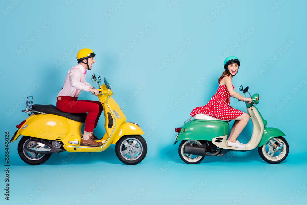 Full body profile side photo of crazy funky energetic two people man woman driver ride motor bike on high speed scream wear red dress shirt pants isolated over blue color background Full body profile side photo of crazy funky energetic two people man woman driver ride motor bike on high speed scream wear red dress shirt pants isolated over blue color background