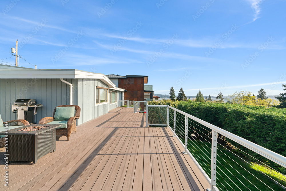 Wicker chairs surrounding a rectangular fire pit on an outdoor wooden deck with a fantastic view of Lake Washington.