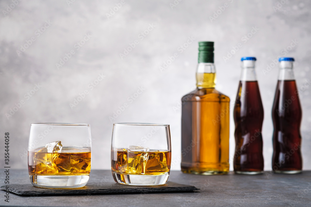 Glass with whiskey and ice cubes on background bottle Glass with whiskey and ice cubes on background bottle