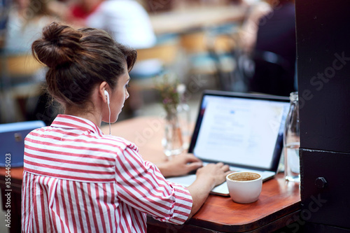young woman typing on a laptop with headphones in her ears at public place. copy space