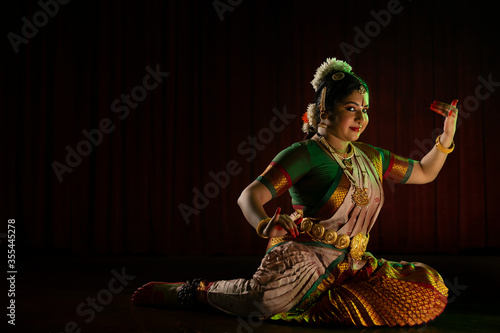 Bharatnatyam dancer playing veena during her performance in front of a dark background. 
 photo