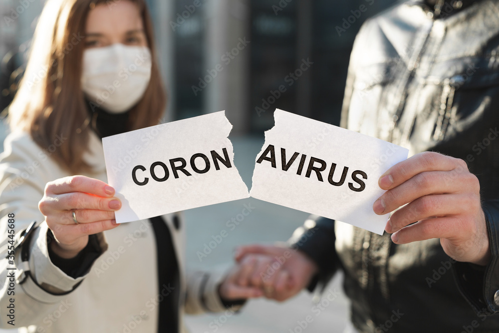 Masked man and woman tear up a paper labeled Coronavirus and hold hands Masked man and woman tear up a paper labeled Coronavirus and hold hands