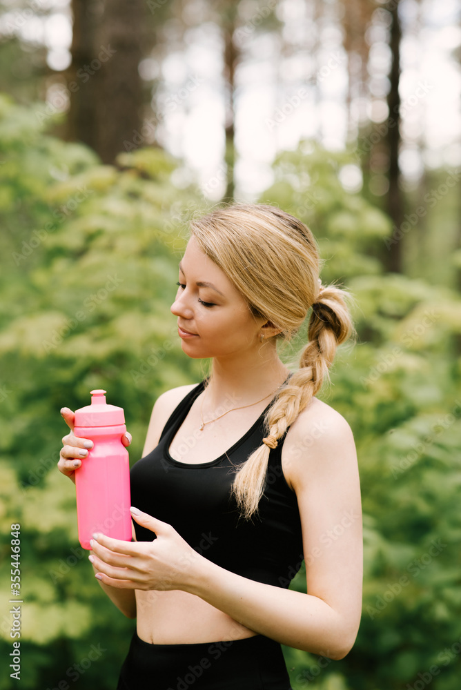 Beautiful young girl in sports uniform with a bottle of water doing yoga and sports in the forest in the open air Beautiful young girl in sports uniform with a bottle of water doing yoga and sports in the forest in the open air