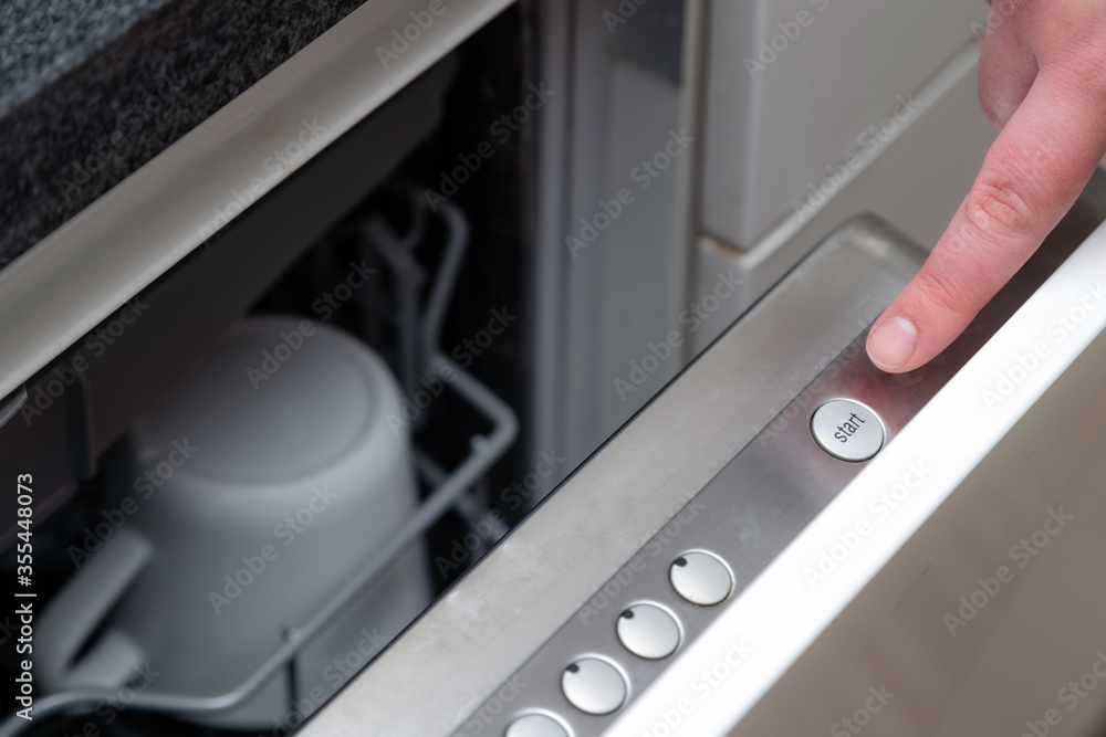 Close up of finger pressing start button on dishwasher in the kitchen. Hand starting dish washer machine Close up of finger pressing start button on dishwasher in the kitchen. Hand starting dish washer machine