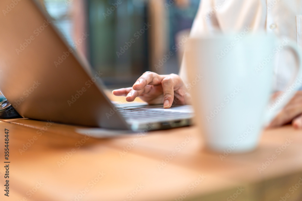 Close up asian man's hand and finger work on his laptop with coffee cup foreground and wood environment furniture... Close up asian man's hand and finger work on his laptop with coffee cup foreground and wood environment furniture...