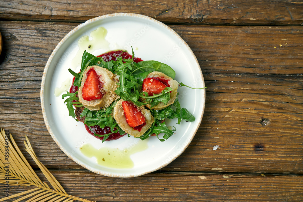 Appetizing toast with goat cheese, red jam, arugula and strawberries with rye bread on a plate on a wooden background Appetizing toast with goat cheese, red jam, arugula and strawberries with rye bread on a plate on a wooden background