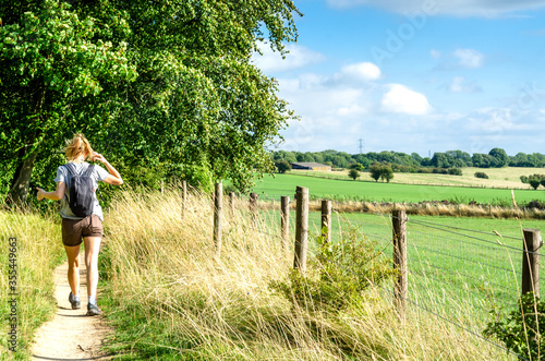 Woman hiking on footpath by agricultural fields. Photo taken on the Cotswold Way in Gloucestershire, England