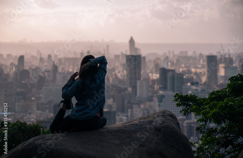 silhouette of woman yoga on the rock with big city in background