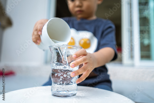 little kid playing and pouring water to glass