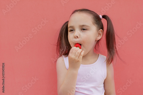 a cheerful girl of 4-5 years old eats fresh strawberries in the fresh air. Summer season. Childhood. Isolated pink background