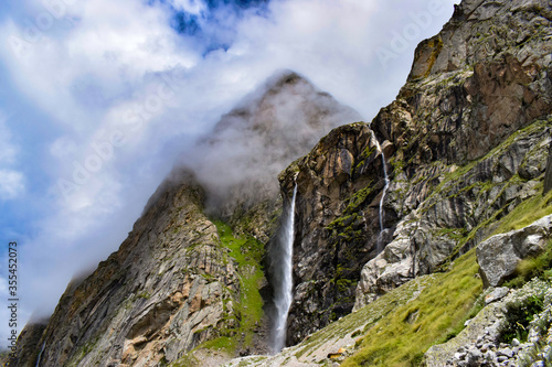 Stunning landscape at roaring Vasudhara falls, people enjoying the fall, big rocky mountains and clouds. Monsoon trek taken in August starts near Mana (last indian village) in Uttarakhand India. photo